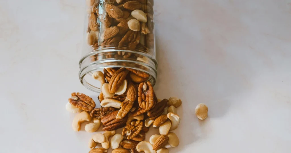 A jar of mixed nuts with some nuts scattered around, offering a protein-packed and nutritious snack